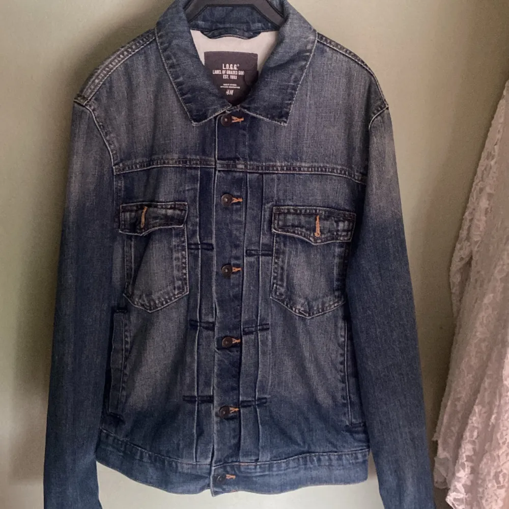 Säljer en snygg jeansjacka från L.O.G.G. av H&M. Den är i klassisk blå denim med knappar framtill och två bröstfickor med lock. Jackan har en normal passform och är perfekt för vår och höst. Den är långärmad och i nyskick. Nypris 349. Jackor.