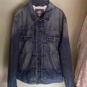 Säljer en snygg jeansjacka från L.O.G.G. av H&M. Den är i klassisk blå denim med knappar framtill och två bröstfickor med lock. Jackan har en normal passform och är perfekt för vår och höst. Den är långärmad och i nyskick. Nypris 349