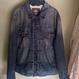 Jeansjacka från L.O.G.G. H&M - Säljer en snygg jeansjacka från L.O.G.G. av H&M. Den är i klassisk blå denim med knappar framtill och två bröstfickor med lock. Jackan har en normal passform och är perfekt för vår och höst. Den är långärmad och i nyskick. Nypris 349