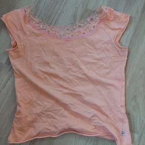 Persikofärgad topp med spets - Strl ca xs/s. Väldigt fin persikofärgad topp som inte används. Fint med spetskant och rosa söm. Skriv vid frågor, pris kan disskuteras