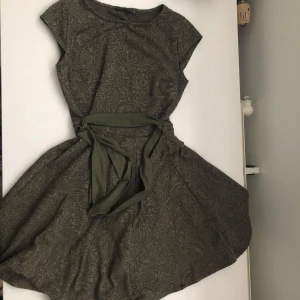 Grön klänning från Atmosphere - Säljer en superfin grön klänning från Atmosphere. Den har ett snyggt mönster och ett knytband i midjan som ger en fin passform. Klänningen är kortärmad och perfekt för både vardag och fest. Passar storlek 36-38.