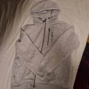 Grå hoodie från Sail Racing - Säljer en snygg och bekväm grå hoodie från Sail Racing. Den har en dragkedja framtill och en justerbar huva. Perfekt för både vardag och chill. Den är i bra skick och supermjuk!