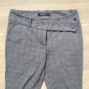 Grå byxor från Stockh LM - Säljer ett par grå kostymbyxor från Stockh LM. De har en elegant design med ett bälte i samma material och knappar för stängning. En knapp saknas, enkel fix. Byxorna har en rak passform och materialet känns mjukt och bekvämt.