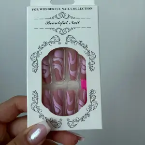 Säljer ett set med superfina lösnaglar i rosa och vitt med ett trendigt swirl-mönster. Perfekt för att snabbt fixa snygga naglar hemma! Setet innehåller flera nagel storlekar och kommer med en nagelfil och klister att tejpa under falska nageln.