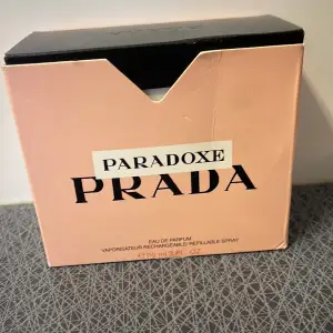 Säljer en elegant och lyxig parfym, Paradoxe från Prada. Förpackningen är i en stilren ljusrosa färg med svart text. Den innehåller 90 ml av en underbar doft som är både påfyllningsbar och i sprayform. Perfekt för den som vill ha en sofistikerad och modern doftupplevelse.