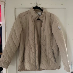 Beige quiltad jacka från Iconic Sport - Säljer en snygg beige quiltad jacka från Iconic Sport i storlek medium. Jackan har en stilren design med dragkedja framtill och praktiska fickor. Perfekt för höst och vår när du vill hålla dig varm och trendig.