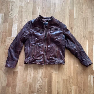 Brun skinnjacka från Rockandblue - Säljer en snygg brun skinnjacka från Rockandblue i storlek XL. Jackan har en cool vintage-look med dragkedja framtill och flera praktiska fickor. Perfekt för höst och vår, och ger en riktigt stilren touch till din outfit. Passar både till vardags och fest!