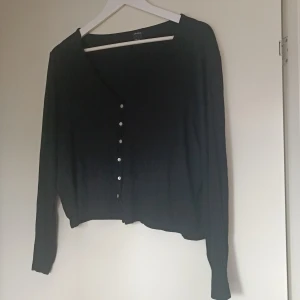 Svart kofta från Lindex - Säljer en stilren svart kofta i kortare modell från Lindex i storlek XXL. Den har långa ärmar och knappar framtill, perfekt för både vardag och fest. Materialet känns mjukt och bekvämt, vilket gör den idealisk för höst och vinter. Ett måste i garderoben!