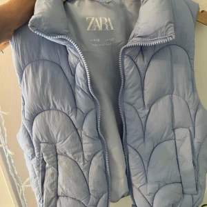 Ljusblå dunväst från Zara - Säljer en superfin ljusblå dunväst från Zara. Den har en quiltad design och dragkedja framtill. Perfekt för lager-på-lager under höst och vår. Västen är i bra skick och väldigt bekväm att ha på sig. Passar perfekt för en casual look eller när du vill hålla dig varm utan att kompromissa med stilen.