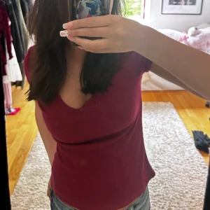 Vinröd ribbad topp - Säljer en snygg vinröd ribbad topp med v-ringning. Toppen är kortärmad och har en tight passform, perfekt för både vardag och fest. Den är i bra skick och superbekväm att ha på sig!