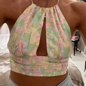 Blommig halterneck topp - Säljer en superfin halterneck topp med blommigt mönster i pastellfärger som rosa, grön och gul. Toppen är croppad och har en snygg öppen rygg med knytband. Perfekt för sommardagar och festivaler!