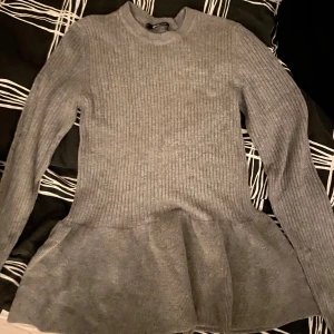 Grå ribbad tröja från Gina Tricot - Säljer en superfin grå ribbad tröja från Gina Tricot. Den har en peplumdetalj i nederkanten som ger en snygg siluett. Tröjan är långärmad och perfekt för både vardag och fest. Passar perfekt till höst och vinter!