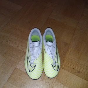 Nike Phantom GT fotbollsskor - Säljer ett par Nike Phantom GT fotbollsskor i storlek herr 42. Skorna är vita med gula detaljer och har snörning. De är i bra skick och perfekta för fotbollsträning eller match.