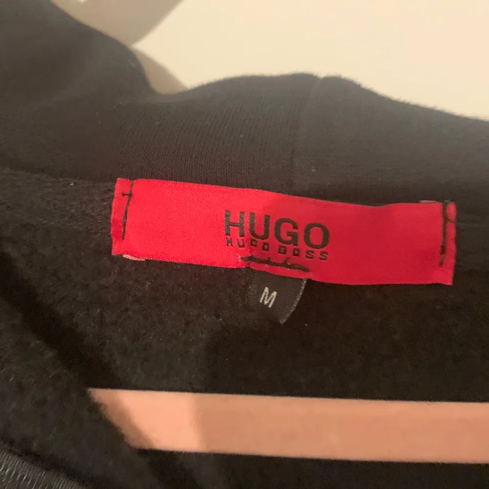 Säljer en stilren svart hoodie från Hugo Boss i storlek M. Den har en dragkedja framtill och en klassisk huva med snören. Perfekt för både vardag och avslappnade tillfällen. Märket syns tydligt på bröstet. Passar perfekt till höst och vinter!. Tröjor & Koftor.