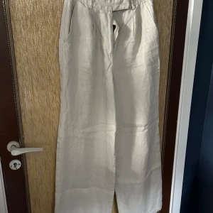 Beige linnebyxor från NA-KD - Säljer ett par snygga och bekväma beige linnebyxor från NA-KD. De är högmidjade med en avslappnad passform och vida ben. Perfekta för en stilren och luftig look. Byxorna har en dragkedja framtill och är gjorda i ett skönt linne-material.