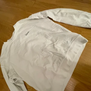 Vit sweatshirt från H&M Divided - Säljer en superfin vit sweatshirt från H&M Divided. Den har en enkel och stilren design med ordet 'love' broderat på bröstet. Tröjan är långärmad och gjord i mjukt bomullsmaterial, perfekt för en avslappnad look. Passar perfekt till både jeans och kjol!