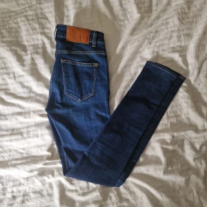 Tiger Of Sweden Jeans - Säljer ett par snygga blå jeans med en cool läderdetalj på baksidan. De har en klassisk femficksdesign och är i ett slitstarkt denimtyg. Perfekta för både vardag och fest!