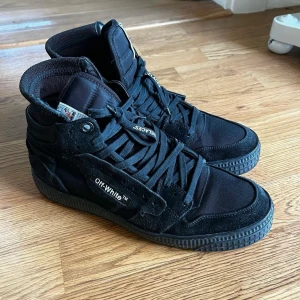 Off-White Court 3.0 - Svart mocka - Svarta sneakers från Off-White med hög design och snörning. Skorna har en robust sula och detaljer i mocka och syntet. Off-White-loggan syns tydligt på sidan.