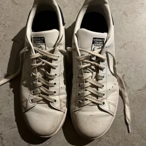 Stan Smith sneakers - Säljer ett par klassiska vita Adidas Stan Smith sneakers med snörning. Skorna har en mörkblå detalj på hälen med logotyp. Tvättar snören och skor innan jag skickar.💗💗