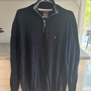 Svart tröja med dragkedja från Oscar Jacobson - Säljer en stilren svart tröja från Oscar Jacobson i storlek XL. Tröjan har en dragkedja vid halsen och en diskret logga på bröstet. Perfekt för en avslappnad men ändå elegant look.