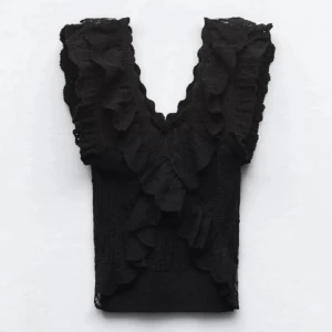 Svart spetsblus med volanger - Snygg svart spetsblus med volanger och v-ringning. Perfekt för en stilfull look. Blusen är ärmlös och har en elegant design som passar till många tillfällen. Använd 1 gång, som ny!