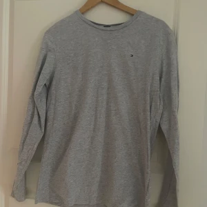 Grå långärmad tröja från Tommy Hilfiger - Säljer en stilren grå långärmad tröja från Tommy Hilfiger i ekologisk bomull. Tröjan har en liten logotyp på bröstet och är perfekt för en avslappnad stil. Passar bra till både jeans och chinos.