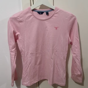 Rosa långärmad tröja från GANT kids - Säljer en rosa långärmad tröja från GANT. Tröjan har en rund halsringning och ett diskret GANT-logotyp broderat på bröstet. Den är inte använd så mycket.