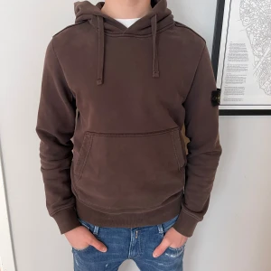 Stone Island Hoodie - Säljer en snygg brun hoodie från Stone Island i skicket 10/10. Modellen är 180cm. Den har knappt använts och äkthetsbevis finns. Mitt pris 999kr nypris 3599kr. Vid frågor så kan ni alltid kontakta mig😄
