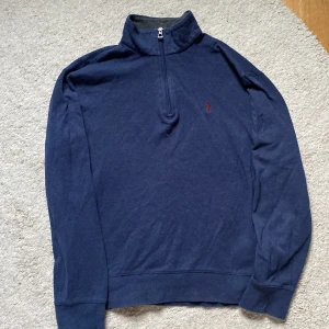 Mörkblå ralph lauren quarterzip - Säljer en stilren mörkblå tröja från Ralph Lauren med halv dragkedja och broderad logga på bröstet. Perfekt för en avslappnad och snygg look. Tröjan har långa ärmar och en bekväm passform.