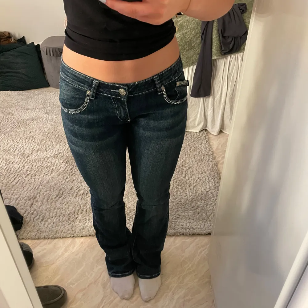 Snygga mörkblå jeans med broderade detaljer på bakfickorna. De har en låg midja och bootcut-stil som ger en klassisk look. Perfekta för en avslappnad stil med en touch av elegans. Supersnygga och knappt använda💕midjemåttet är 42cm, jag är 168 och dom är perfekt längd på mig, jag skulle säga att dom är längd 34. Några stenar baktill saknas, men inget man tänker på (se bild 2) 💞. Farkut & Housut.
