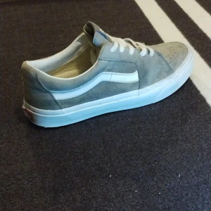 Grå sneakers från Vans - Säljer ett par grå sneakers från Vans med vit sula och snörning. Skorna har en klassisk design med Vans-logga på hälen och tungan. Perfekta för en avslappnad stil.