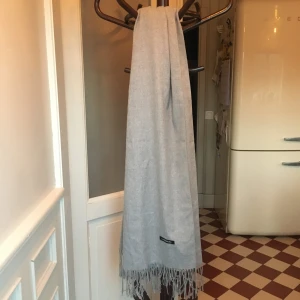 Grå halsduk med fransar - Snygg och stilren grå halsduk med fransar från Cashmerelike. Perfekt för att hålla dig varm under kyliga dagar. Den mjuka känslan ger en lyxig touch till din outfit.