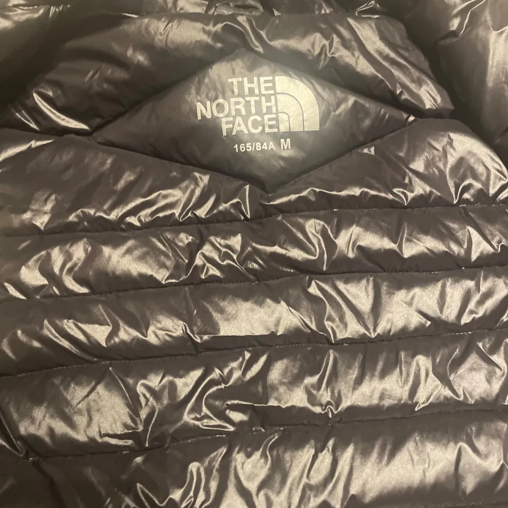 Säljer en svart dunväst från The North Face. Västen har en dragkedja framtill och två praktiska fickor med dragkedjor. Perfekt för kyligare dagar när du vill hålla värmen utan att bära en jacka.. Takit.