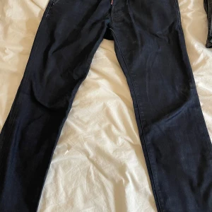 Svarta jeans från Dsquared2 - Snygga svarta jeans från Dsquared2 med klassisk femficksdesign. De har en diskret logga på bakfickan och en röd etikett vid gylfen. Perfekta för en stilren look. 