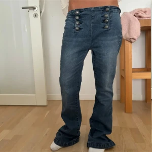 Blå jeans med knappar - Snygga blå jeans med hög midja och unika knapprader framtill. Byxorna har en bootcut-stil som ger en trendig look. Perfekta för att ge din outfit en cool touch.