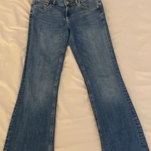 Blå bootcut jeans - Snygga blå low waist bootcut jeans med klassisk femficksdesign. Kommer inte till användning och säljs inte längre. I mycket bra skick och har inga defekter. Bra längd på mig som är 173 cm lång men passar även bra till kortare.