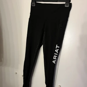 Svarta leggings från Ariat - Snygga svarta leggings från Ariat med medel midja och logotyp på benet. Perfekta för ridning med bekväm passform och stretchigt material💞