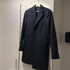 Mörkblå kappa från Riley - Snygg mörkblå kappa från Riley i en mix av ull och kashmir. Den har en klassisk design med långa ärmar och en stilren krage. Perfekt för att hålla sig varm och elegant under kyligare dagar.