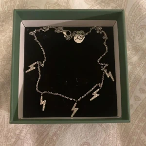 Silverhalsband med blixtar från Edblad - Snyggt silverhalsband från Edblad med flera små blixtar dekorerade med glittrande stenar. Perfekt till både vardag och fest. Halsbandet har en tunn kedja och ett hänger vid låset med edbladsmärke