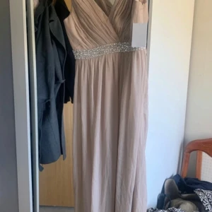 Beige rosa långklänning från Chiara Forthi strl 38 - Elegant beige / rosa långklänning från Chiara Forthi med v-ringad design och glittriga detaljer i midjan. Perfekt för speciella tillfällen med sin flytande och stilrena look.