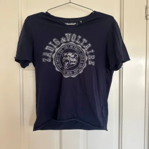  Zadig & Voltaire T-shirt  - Snygg blå t-shirt från Zadig & Voltaire med ett coolt tryck på! Den är från barnavdelningen o är största storlek där ifrån så skulle säga den passar XS/S🥰😇😇