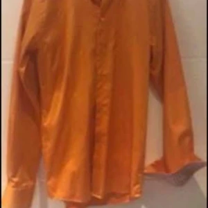 Orange långärmad skjorta - Snygg orange skjorta med långa ärmar och klassisk krage. Perfekt för att liva upp garderoben med en färgklick. Skjortan har knappar framtill och är tillverkad i ett lätt material som passar bra till olika tillfällen. Säljer Eton skjorta. Använd max 3 gånger. Storlek: 38, vilket motsvarar S. Den är SLIM i modellen.