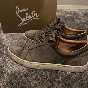 Grå sneakers från Christian Louboutin - Snygga grå sneakers i mocka från Christian Louboutin med den ikoniska röda sulan. Skorna har snörning och en stilren design som passar perfekt för en trendig look. Skick 6,5 av 10 men går att ordna med hjälp av sko rengörings kitt. Det finns inga ytliga skador utan dem bör bara få ett bra omhändertagande🤩