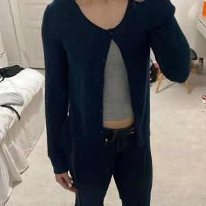 Mörkblå kofta - Säljer en stilren mörkblå kofta med knappar framtill. Koftan har en u-ringad design och långa ärmar, perfekt för en avslappnad look.