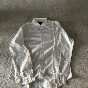 Vit skjorta från Ralph Lauren - Säljer en klassisk vit skjorta från Ralph Lauren med broderad logga på bröstet. Skjortan har långa ärmar och knappar framtill. Perfekt för en stilren look. Riktigt bra skick nästan som ny. Storlek L