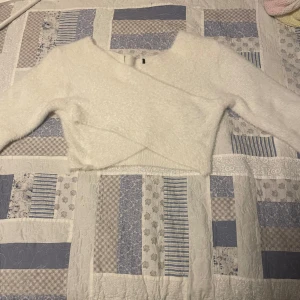 Vit fluffig omlottopp - Säljer en supermjuk och fluffig vit omlottopp. Den är croppad och har långa ärmar, perfekt för en mysig dag eller en chill fest. Toppen är i bra skick och passar perfekt till höst- och våroutfits. Den har en snygg omlottdesign som ger en fin detalj till din look. 🤍