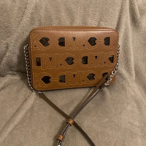 Brun axelväska från Michael Kors - Säljer en snygg brun axelväska från Michael Kors med ett coolt utskuret mönster och kedjedetaljer. Perfekt för både vardag och fest! Väskan har en justerbar rem och är i mycket bra skick. Passa på att köpa denna stiliga accessoar! Jag har använt bara 2 gånger. Pris kan diskutera!