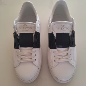 Valentino open - Säljer ett par snygga Valentino Garavani sneakers i vitt med svarta detaljer. Skorna har en stilren design med snörning och är i bra skick, men med lite smuts på sulorna. Perfekta för både vardag och fest! 🖤🤍kommer utan låda då jag köpte dom här på plick utan låda. Pris ej hugget i sten