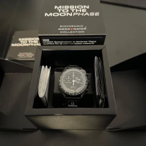 Omega x Swatch Speedmaster Mission to the Moonphase - Säljer en helt ny oanvänd Omega x Swatch Speedmaster från Mission to the Moonphase-kollektionen. Klockan har en elegant svart design med detaljerad urtavla och tachymeter. Perfekt för både vardag och speciella tillfällen. Levereras i originalförpackning. Kvitto samt original påse finns.