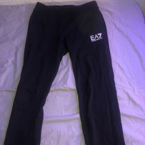 Svarta byxor från Emporio Armani - Säljer ett par svarta byxor från Emporio Armani i storlek 12A. Byxorna är i bra skick och har en stilren design med EA7-logga på sidan. Perfekta för både vardag och avslappnade tillfällen. Materialet känns mjukt och bekvämt.